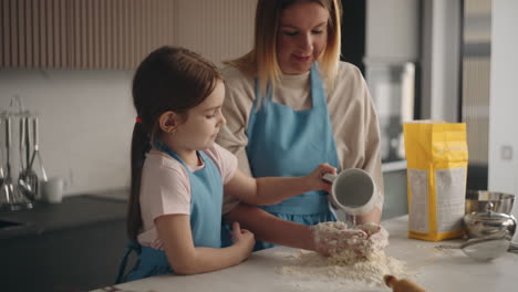 Kleines-Mädchen-Hilft-Ihrer-Mutter,-Teig-Für-Kuchen-Zu-Machen,-Indem-Sie-Wasser-Auf-Mehl-Gießt,-Frau-Knetet-Mit-Den-Händen